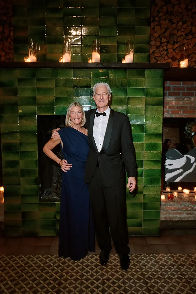 A couple by the green-tiled fireplace, lit by candles.